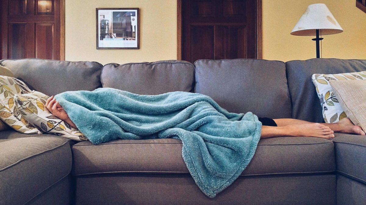 person sleeping on a couch covered in a blue blanket