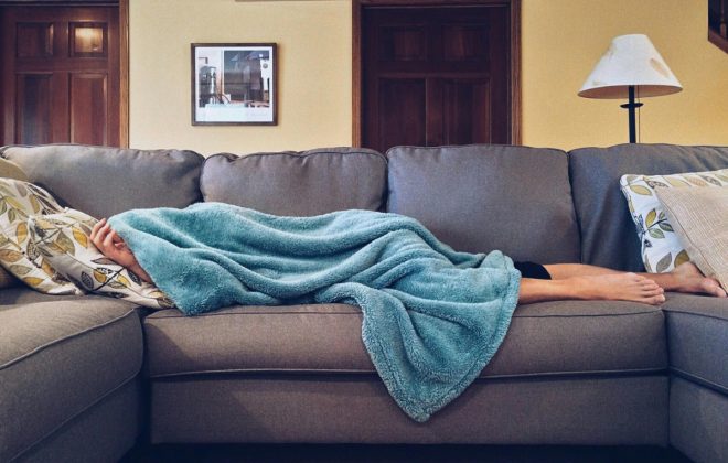 person sleeping on a couch covered in a blue blanket