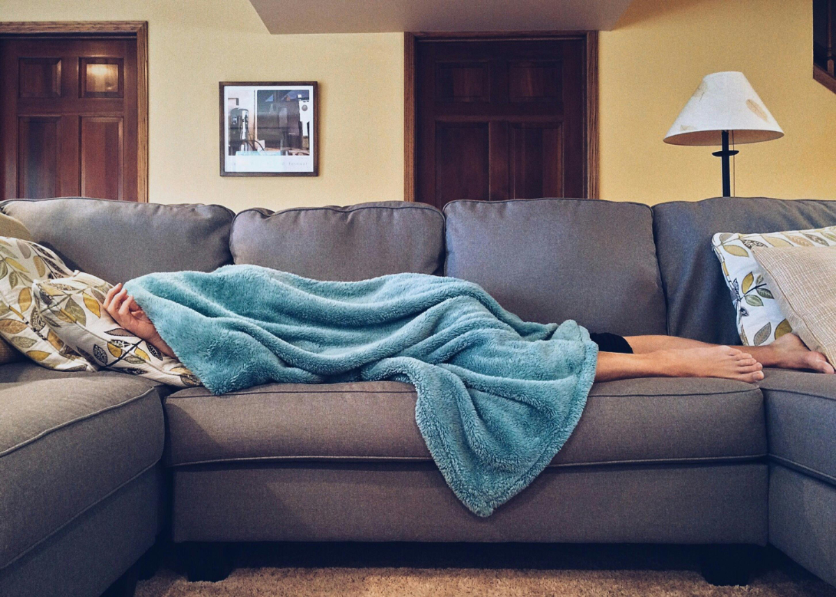 person sleeping on a couch covered in a blue blanket